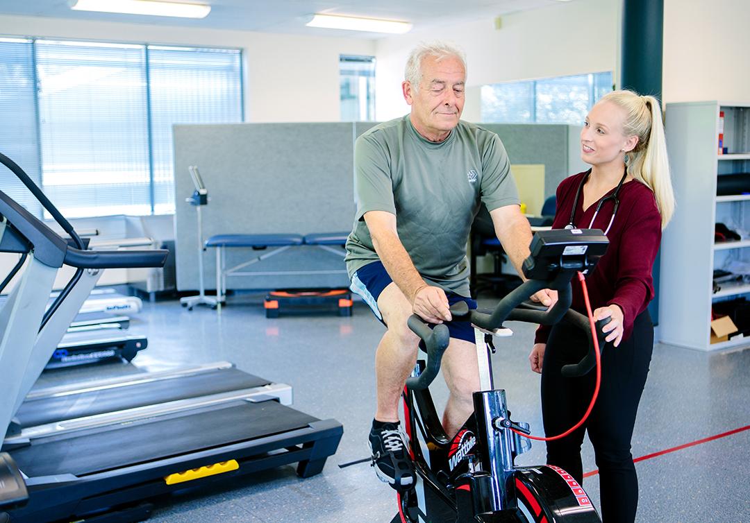 Student helping patient with rehab on stationary bike