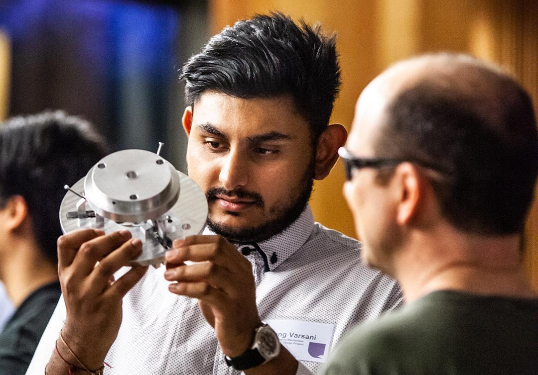 Man holding metal object while talking to another man. 