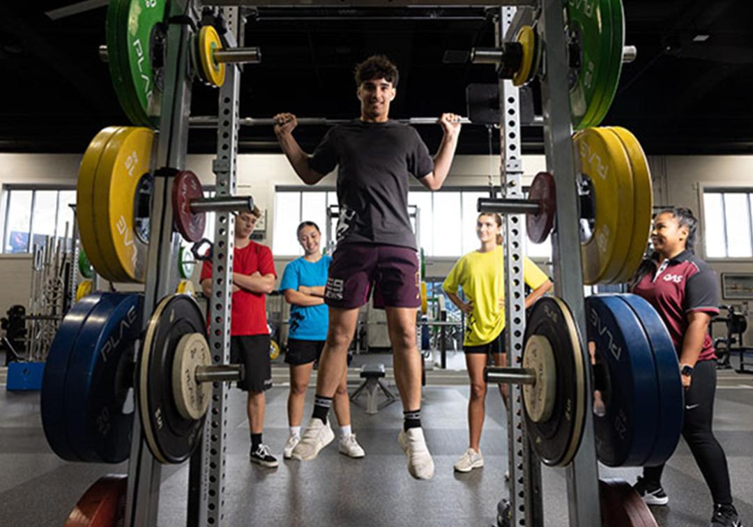 A man uses weight lifting equipment while others watch on.