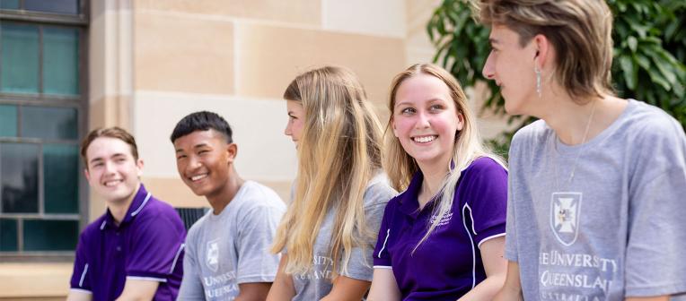 Students sitting on a wall in purple and grey tshirts chatting