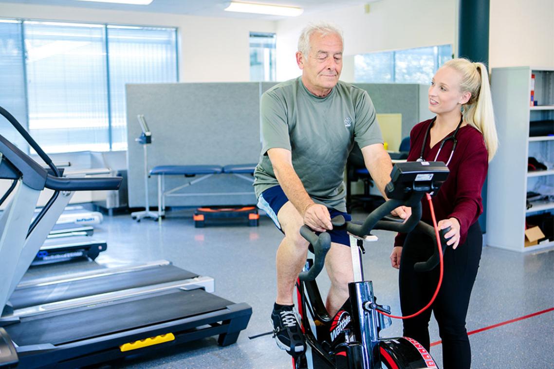 Physio student assisting male patient complete a workout on an exercise bike