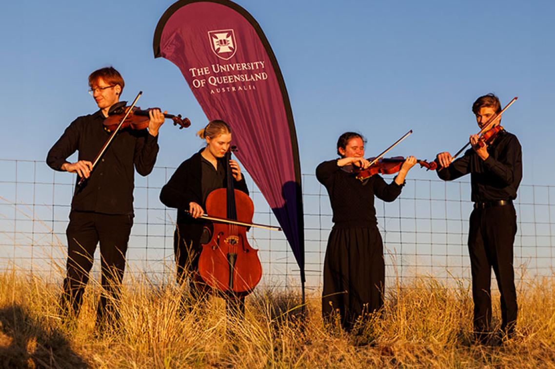 4 musicians playing in a field of long yellow grass against the blue sky. 