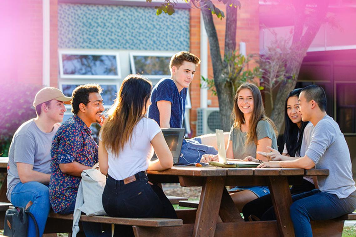 Students sitting at picnic table is grassy courtyard. 