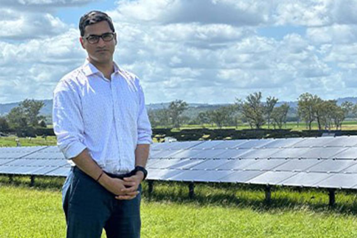 Man stands in front of solar panels in field.