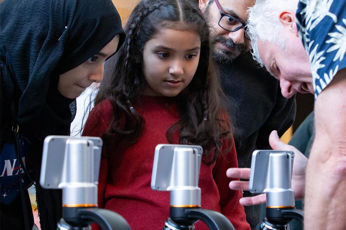 Group of adults and children standing around microscopes 