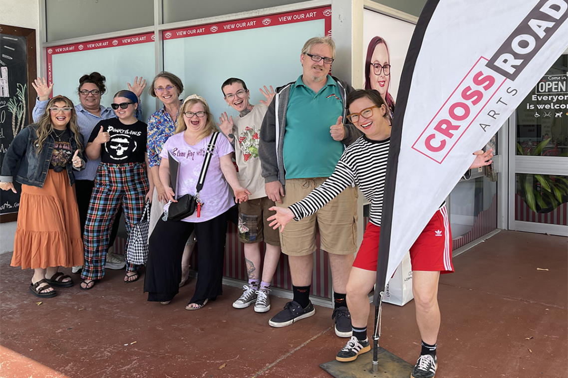 A group of people standing outside a building, one of them holding a sign reading "crossroad arts"