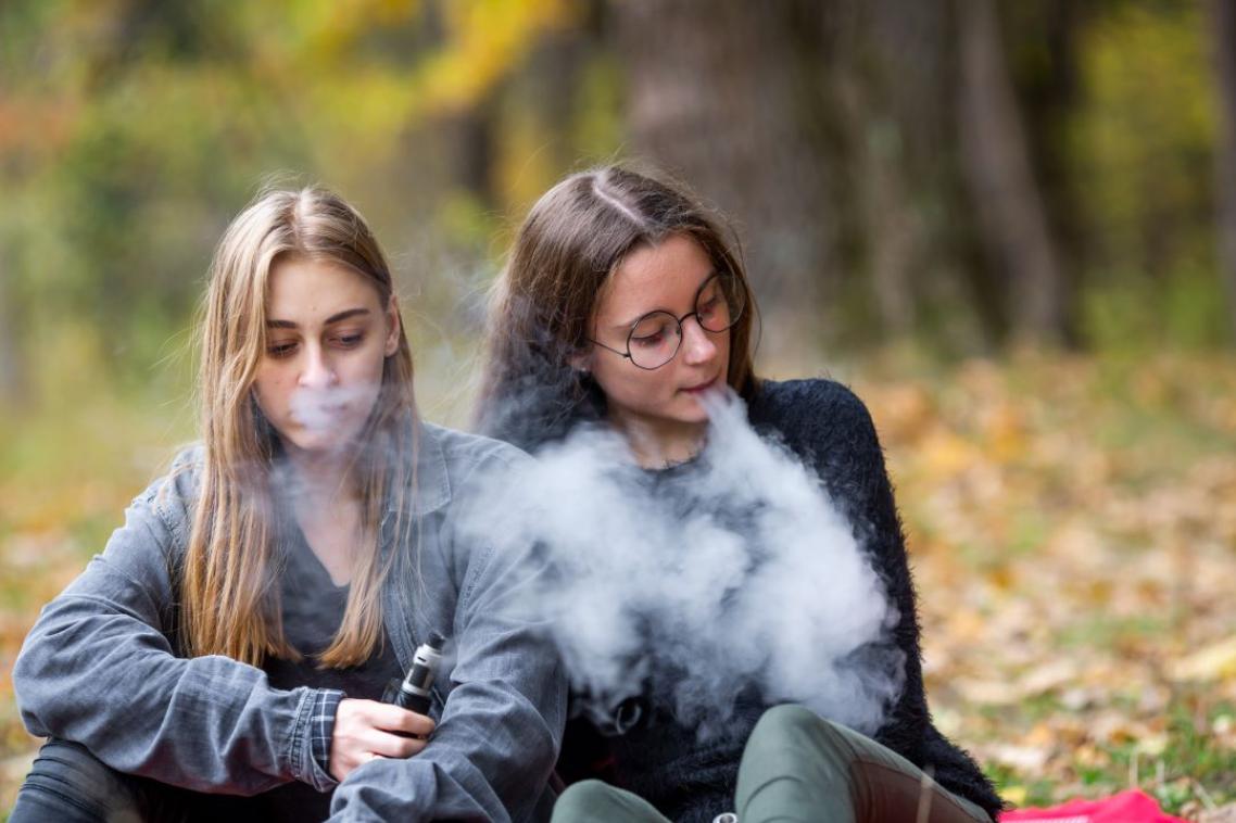 Two young girls sitting in an outdoor area, a big cloud of smoke around them 